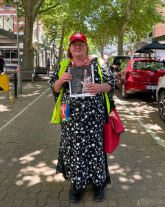 Vendor Lynn in her Big Issue uniform holding her vendor profile.