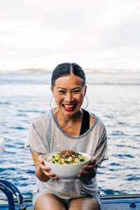 Poh smiling excitedly by the sea, holding a bowl of her famous laksa.