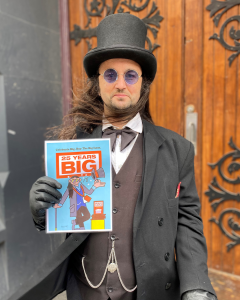 Vendor Daryl holding a print out of his illustration. He's wearing a top hat and round purple glasses.